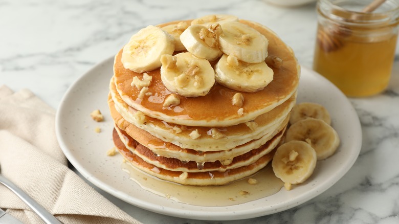 Delicious pancakes with bananas, walnuts and honey on a plate on a counter.