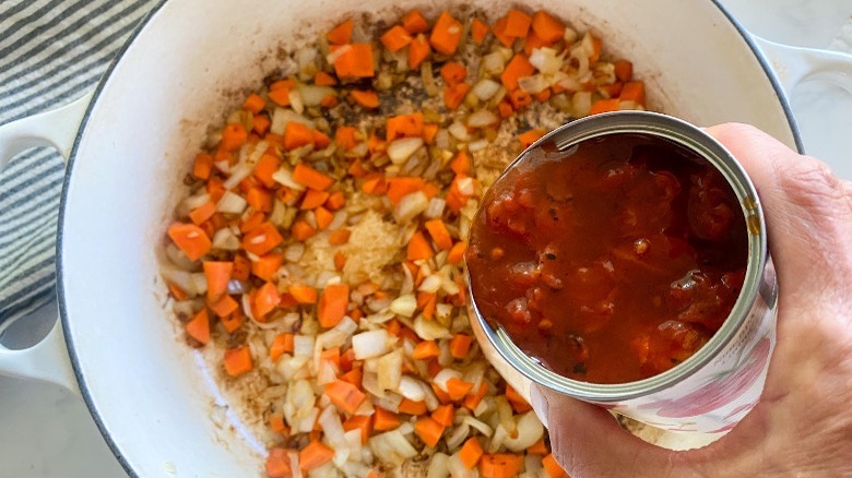 pouring canned tomatoes into pot