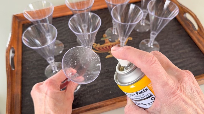 Spraying mini champagne flutes with non-stick cooking spray on tray