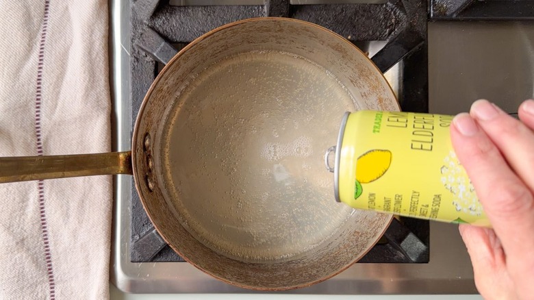 Pouring lemon elderflower soda into saucepan on stovetop