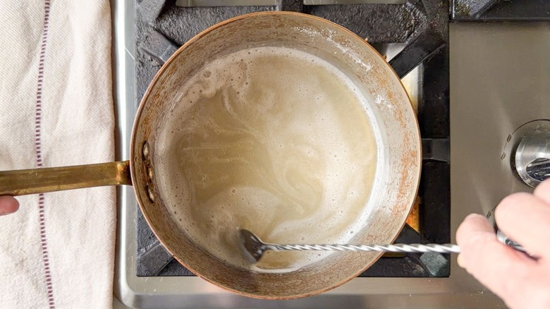 Stirring gelatin and soda in saucepan with long spoon on stovetop