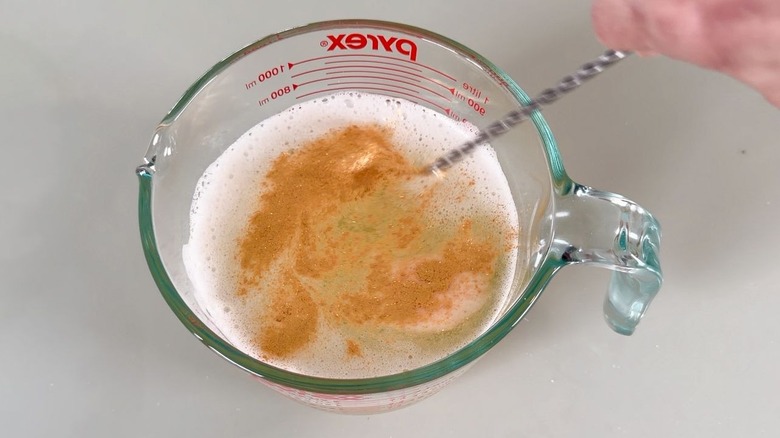 Stirring edible gold glitter into champagne jell-o shot mixture in glass measuring pitcher