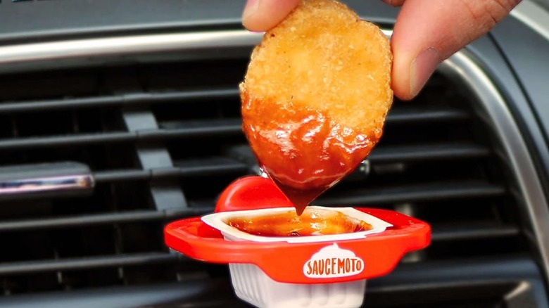 Fingers dip chicken nugget into saucemoto holder attached to car vent