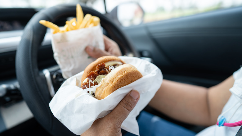 Person holds a hamburger and french fries while sitting in drivers seat