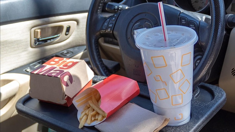 Tray with fast food and drink on it attached to steering wheel