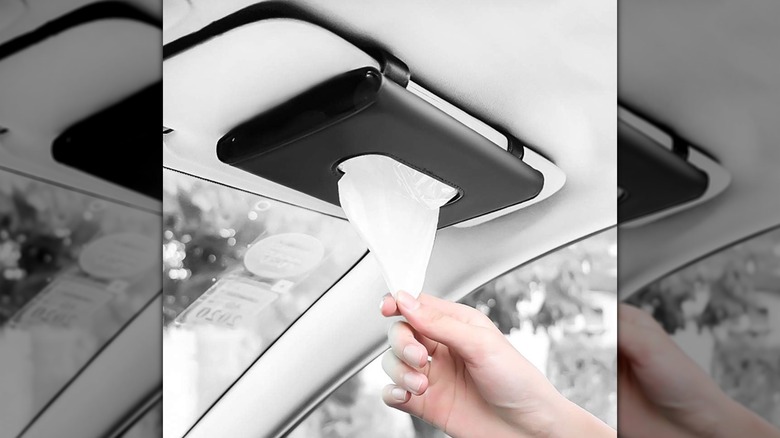 hand pulling napkin from holder attached to car sun visor