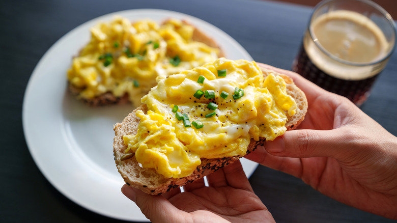 Hands holding slice of toast with scrambled egg
