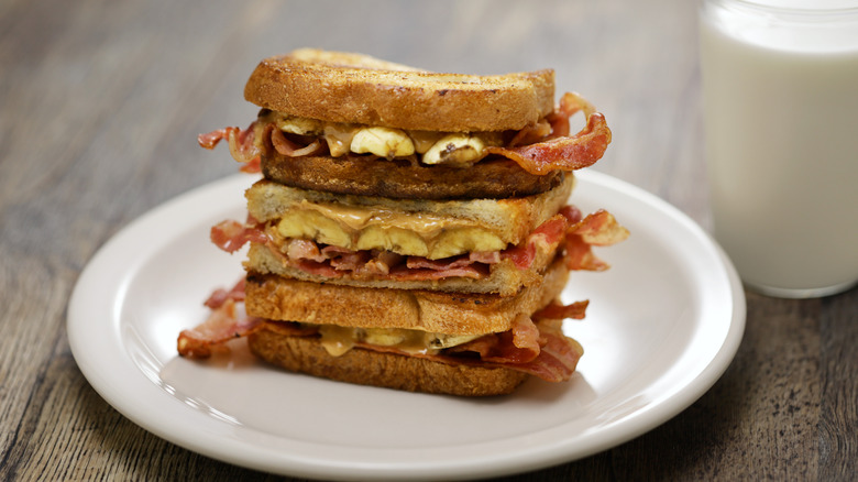 A stack of fried peanut butter, banana, and bacon sandwiches, with a glass of milk