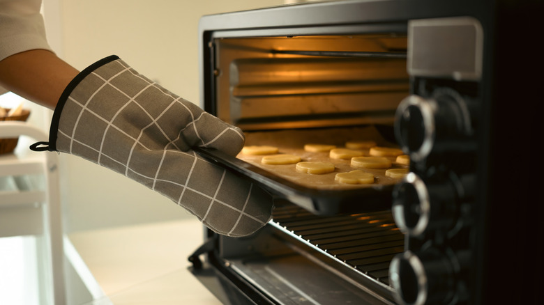 A person wearing oven mitts putting a tray full of cookies in an oven