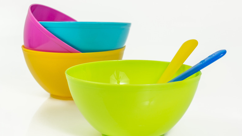 A bunch of colorful plastic bowls with spoons on a white table