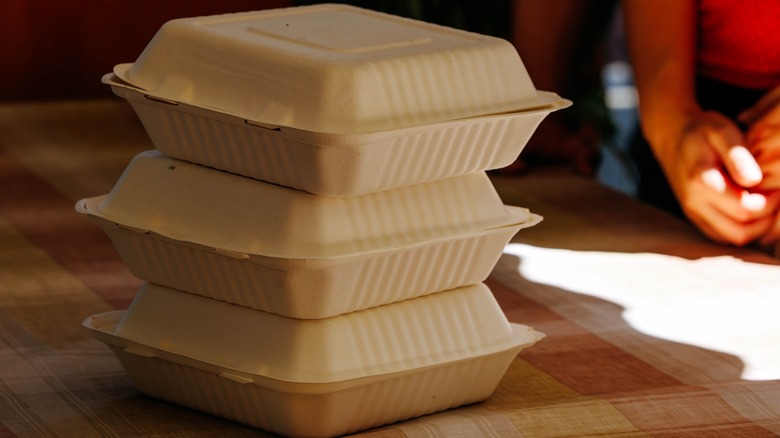 Three Styrofoam takeout containers stacked on top of one another on a wooden table