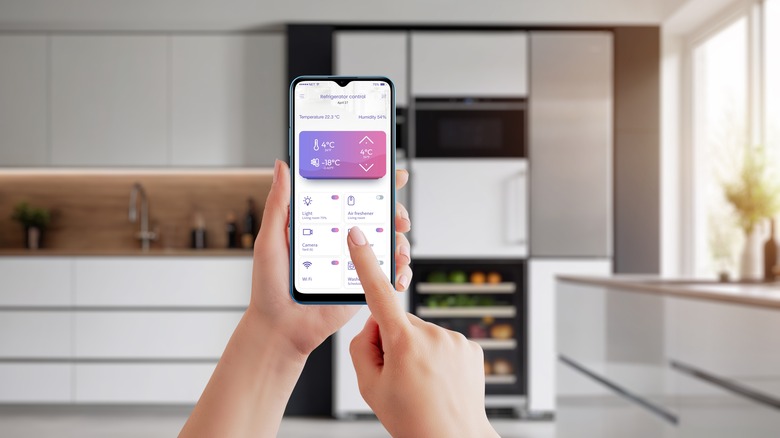 Person holding a smart phone, touching a screen with a refrigerator app pulled up