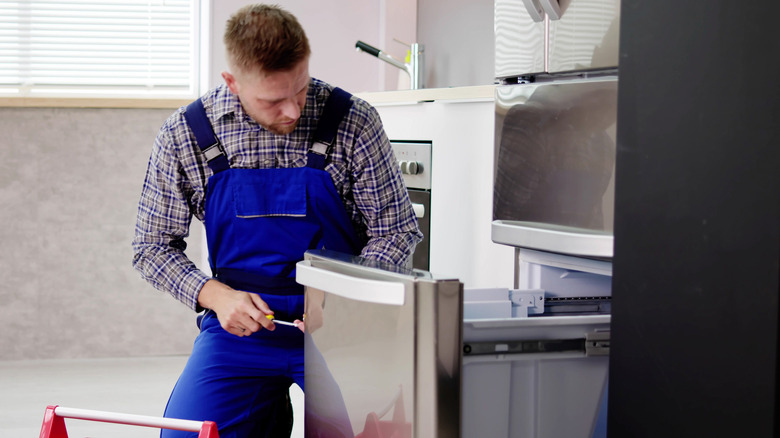 A repairman in blue coveralls tightens a screw on a freezer door