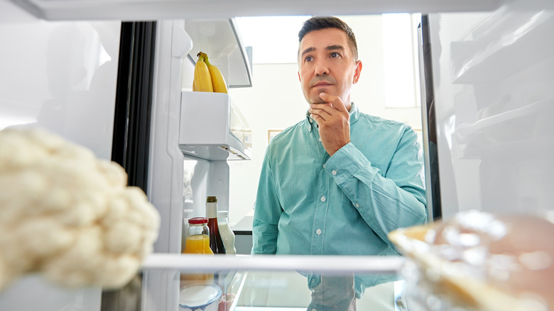 View from inside a fridge with a man scratching his chin while deciding what to eat