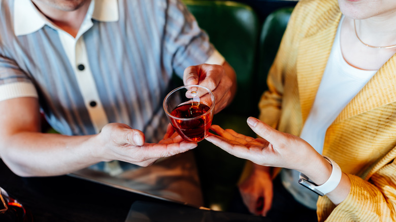 A close up of someone handing a cocktail in a mug to someone else