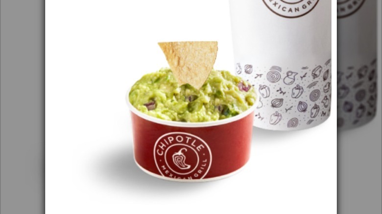 a cup of Chipotle guacamole with a chip sticking out of the top with a drink