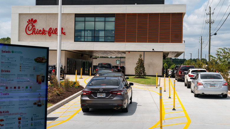 Chick-fil-A restaurant with two drive thru lanes full of cars, and a Chick-fil-A menu board in the foreground