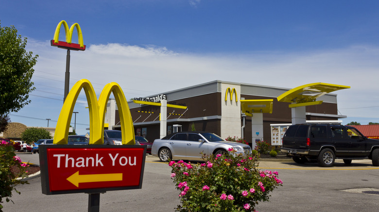 McDonald's restaurant with multiple cars in its drive thru, with a "Thank You" sign with the Golden Arches in the foreground