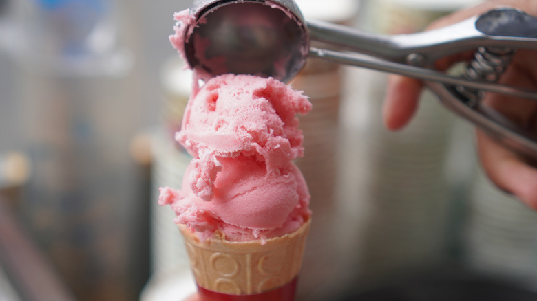 Strawberry ice cream being scooped onto a cone