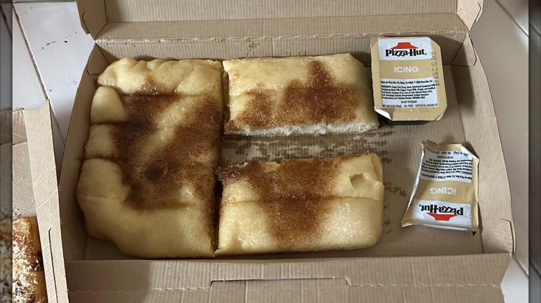 A box of Pizza Hut Cinnamon Sticks, with a carton of icing on the side