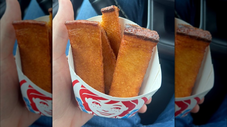 A hand holds a carton of Wendy's French Toast Sticks