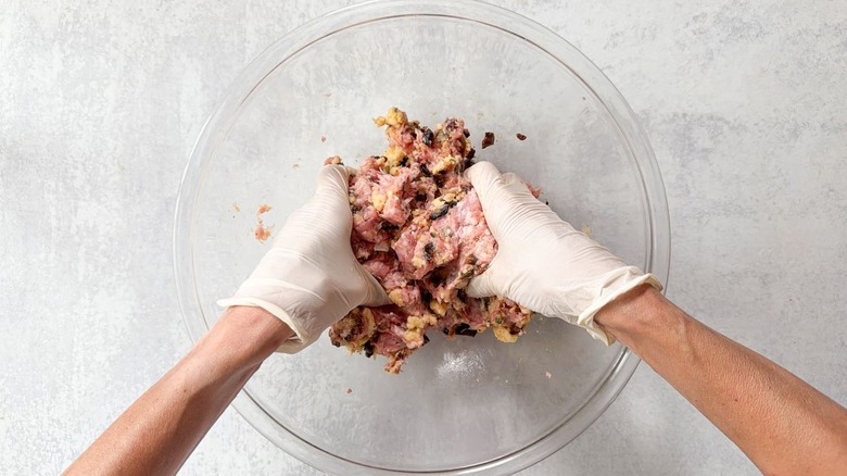 Mixing meatball ingredients together by hand wearing gloves in large glass bowl