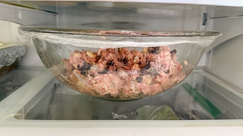 Fig and gorgonzola meatball mixture in plastic-covered glass bowl in refrigerator