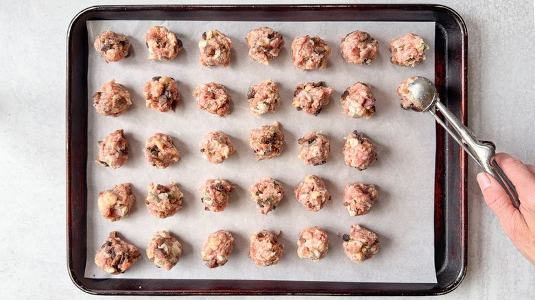 Scooping meatball mixture with cookie scoop onto parchment-lined baking sheet