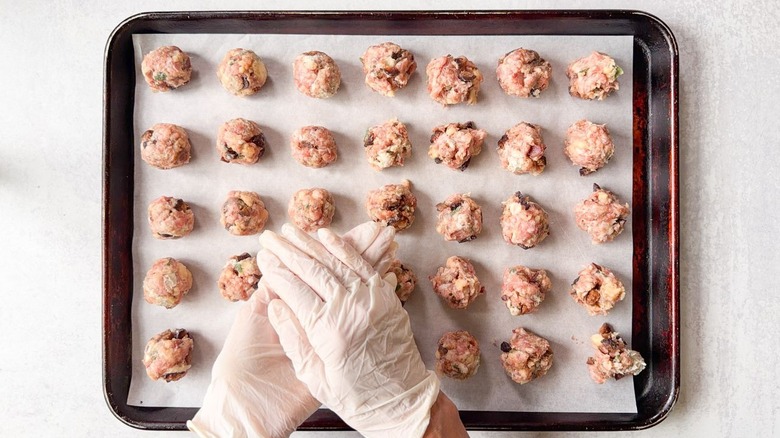 Rolling meatballs by hand onto parchment-lined baking sheet wearing gloves