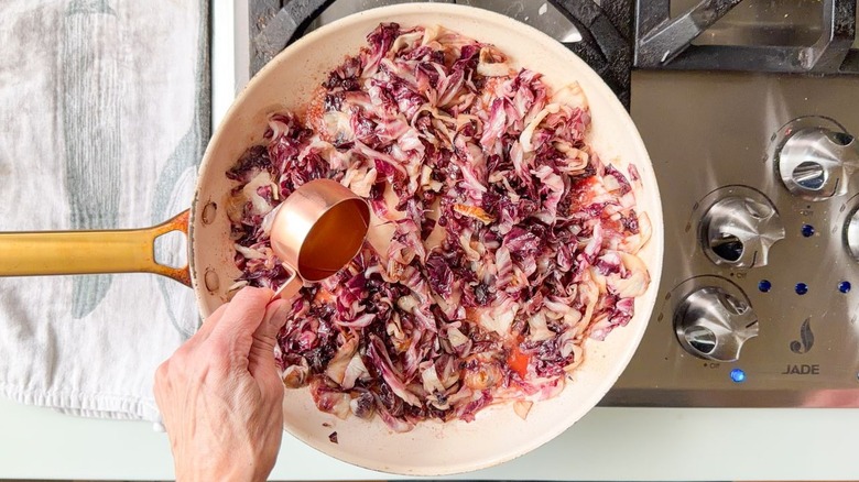 Adding chicken stock to charred radicchio in skillet on stovetop
