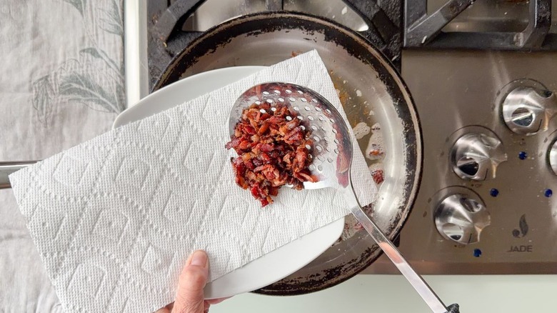 Using slotted spoon to remove chopped bacon from skillet
