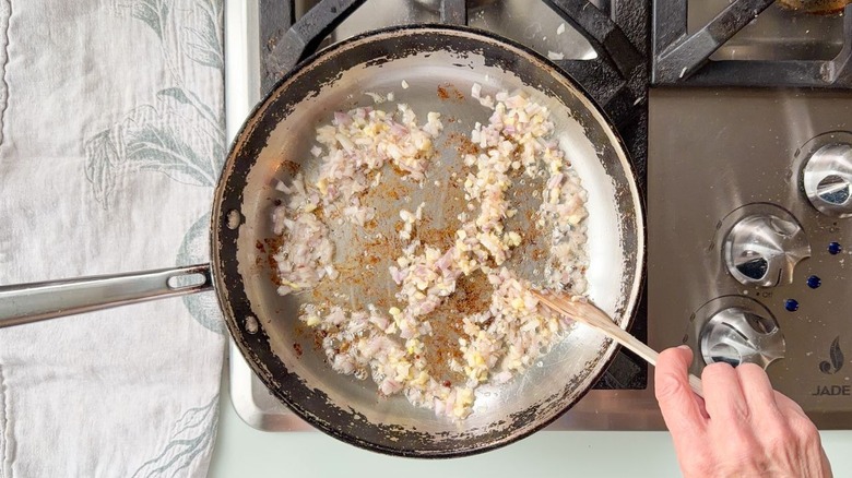 Sautéing minced shallot and garlic in bacon fat with wooden spoon in skillet