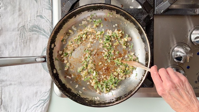 Sauteing chopped sage, thyme, shallots, and garlic in skillet with wooden spoon