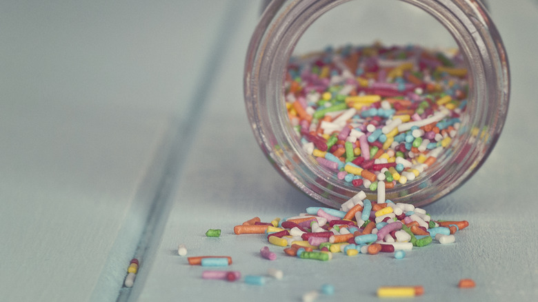A bottle of rainbow sprinkles tipped over on its side with sprinkles spilling out.