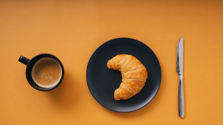 A croissant in a plate next to coffee 