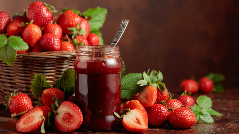 Fresh strawberries in a basket and surrounding a glass jar of jam