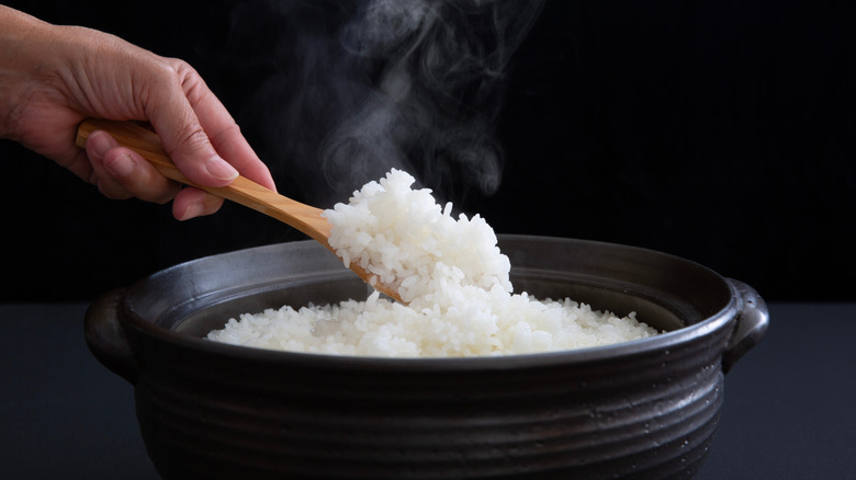 A spoonful of rice in a black container with steam rising off of it