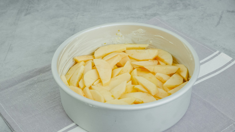 Slices of apple in bottom of a white buttered baking dish