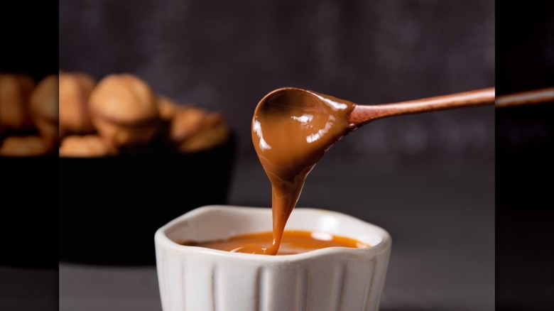 caramel trickling from a wooden spoon into a white container