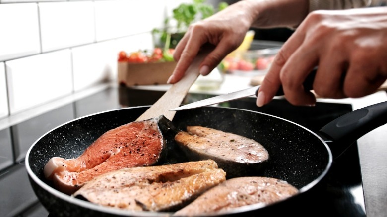 a woman pan-frying four pieces of fish