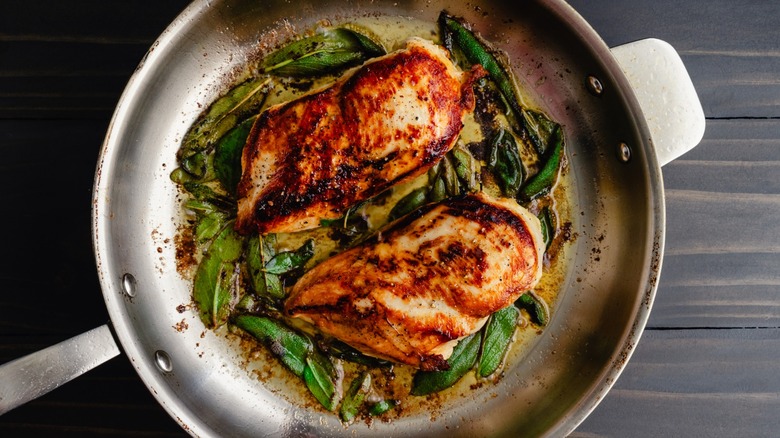 chicken and herbs cooking in a stainless steel skillet