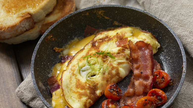 Omelet in frying pan with bacon and tomatoes