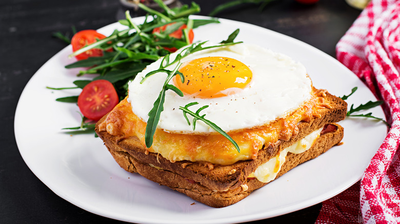 A croque madame on a white plate with arugula and cherry tomatoes