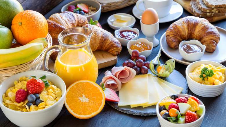 Table with many different breakfast foods, like croissants, jam, meat, cheese, cereal, and fruit