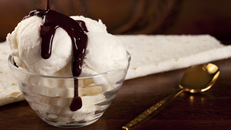 Chocolate syrup is drizzled onto a bowl of vanilla ice cream.