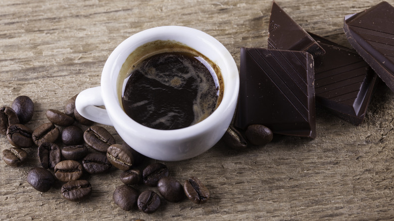 Coffee in a cup with chocolate and beans beside it
