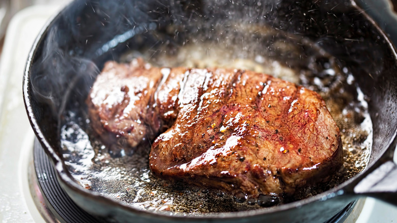 An angus steak frying in a cast iron pan