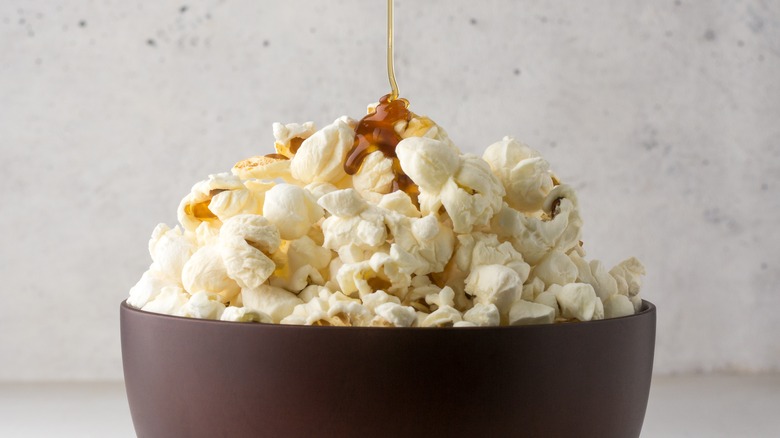 A spoon drizzling honey on a bowl of popcorn