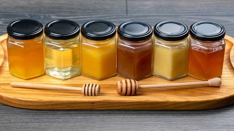 Jars of different types of honey and a honey stick