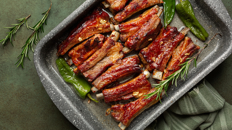 Oven tray with baked ribs surrounded by peppers and parsely